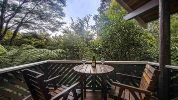 Una terraza de madera con una mesa redonda y sillas, rodeada de abundante vegetación y árboles.
