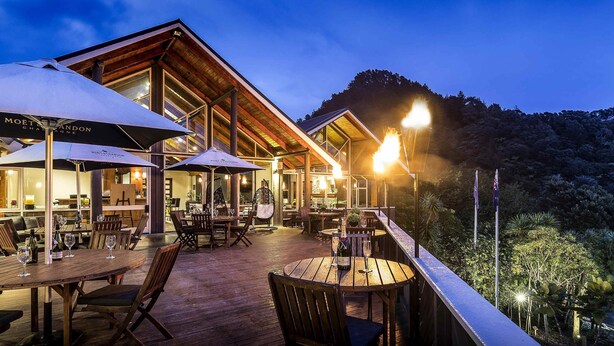 Un espace de restauration en plein air avec des tables et des chaises en bois, des parasols et une vue sur la forêt environnante.