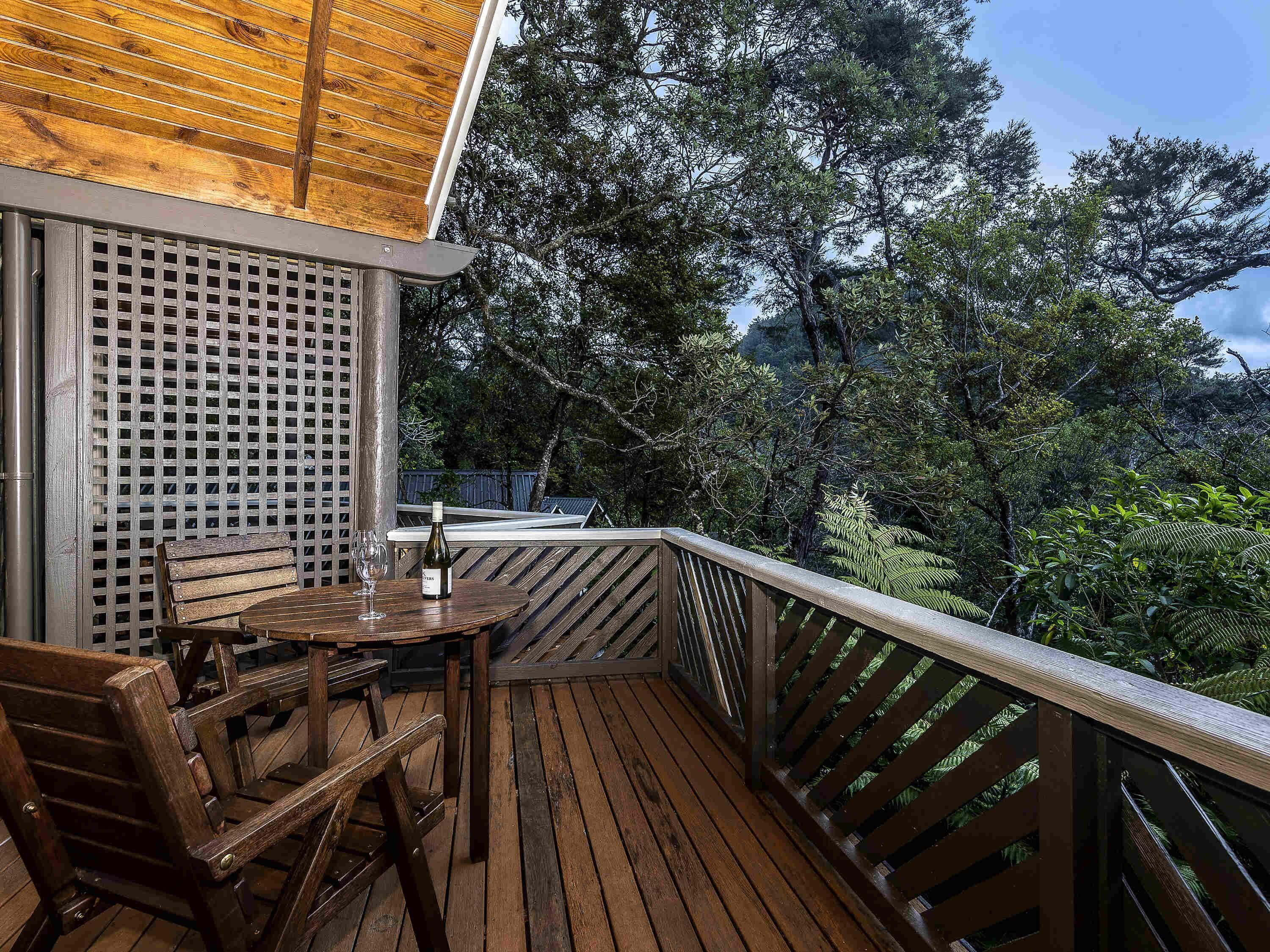 Terraza de madera con mesa y sillas, con vistas a un área boscosa.