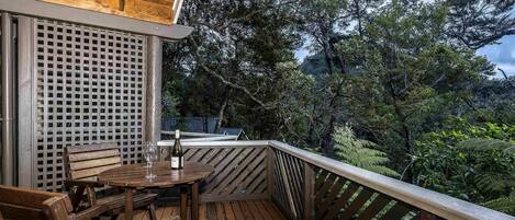 Terraza de madera con mesa y sillas, con vistas a un área boscosa.