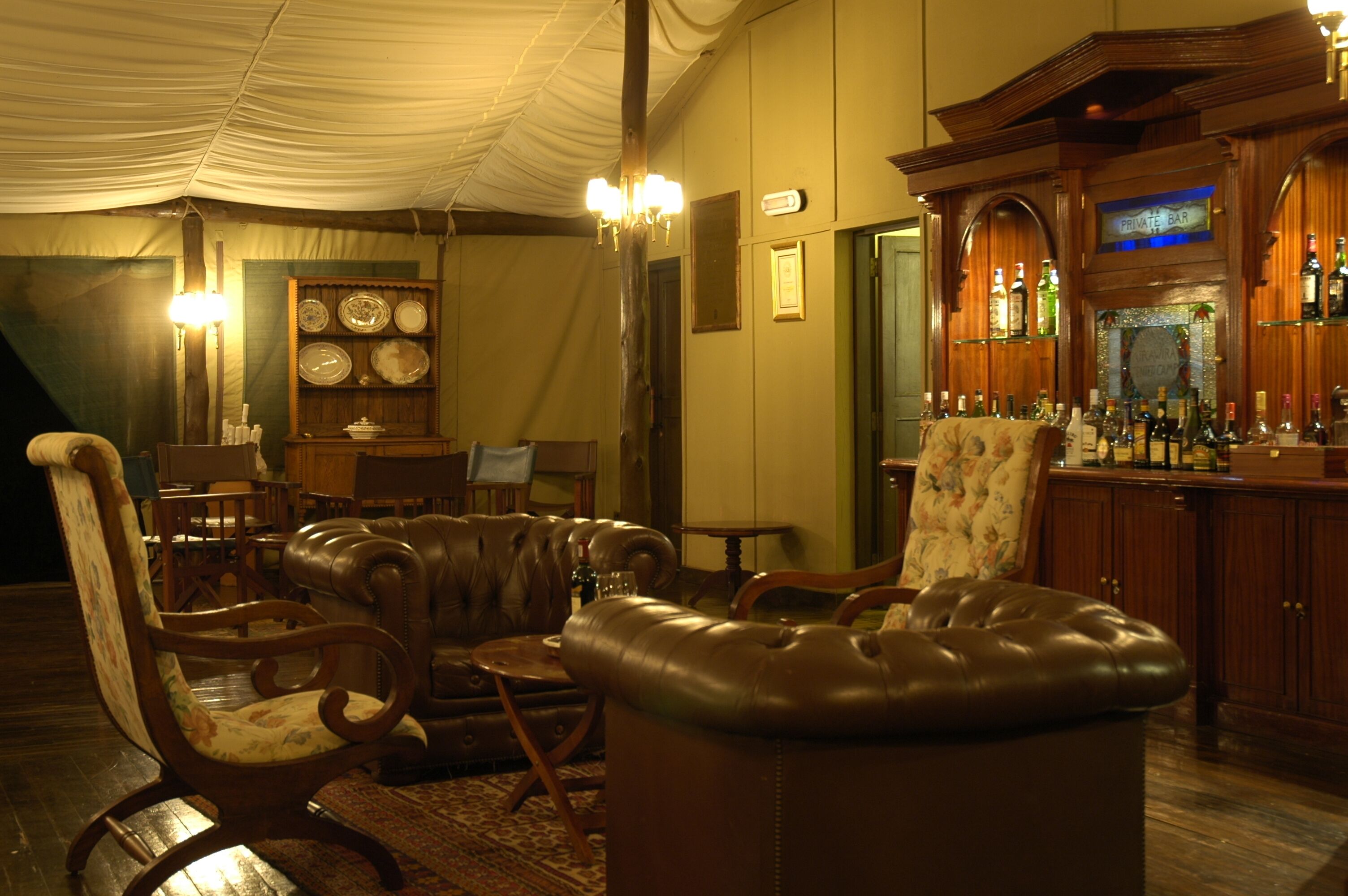 A cozy lounge area with leather furniture, a bar with bottles, and a wall-mounted clock.
