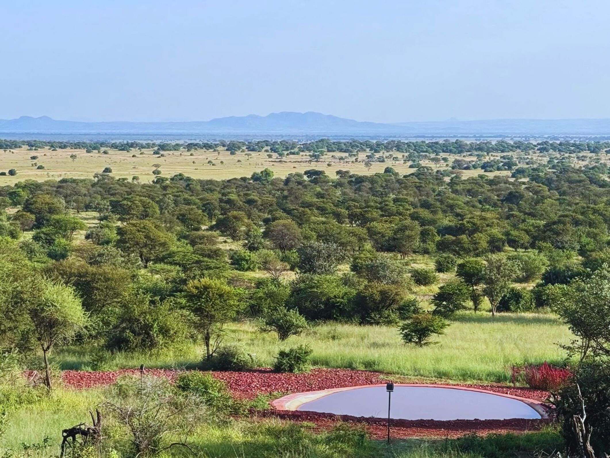 A landscape with a circular water feature surrounded by a red border, trees, and distant mountains.