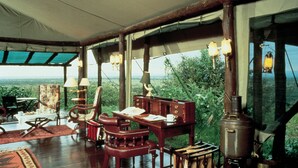 A rustic wooden room with a large table, chairs, and a vintage stove. - Kirawira Serena Camp (Serengeti)