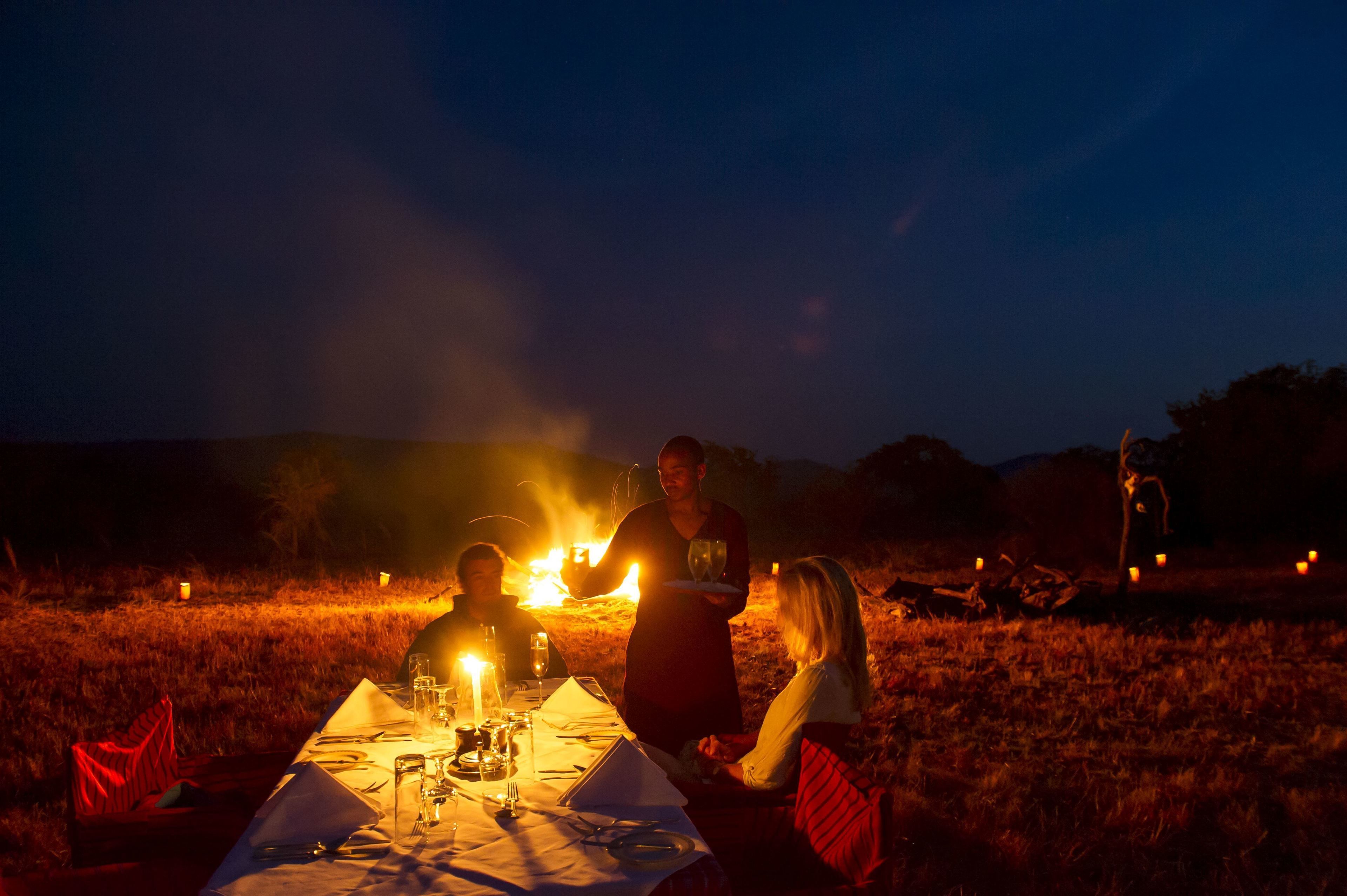 Une table dressée à l’extérieur, avec un feu en arrière-plan.