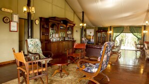 A spacious room with wooden furniture, a bar area, and a large window with curtains. - Kirawira Serena Camp (Serengeti)