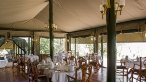 A tented dining area with tables set for service, wooden chairs, and hanging light fixtures. - Kirawira Serena Camp (Serengeti)