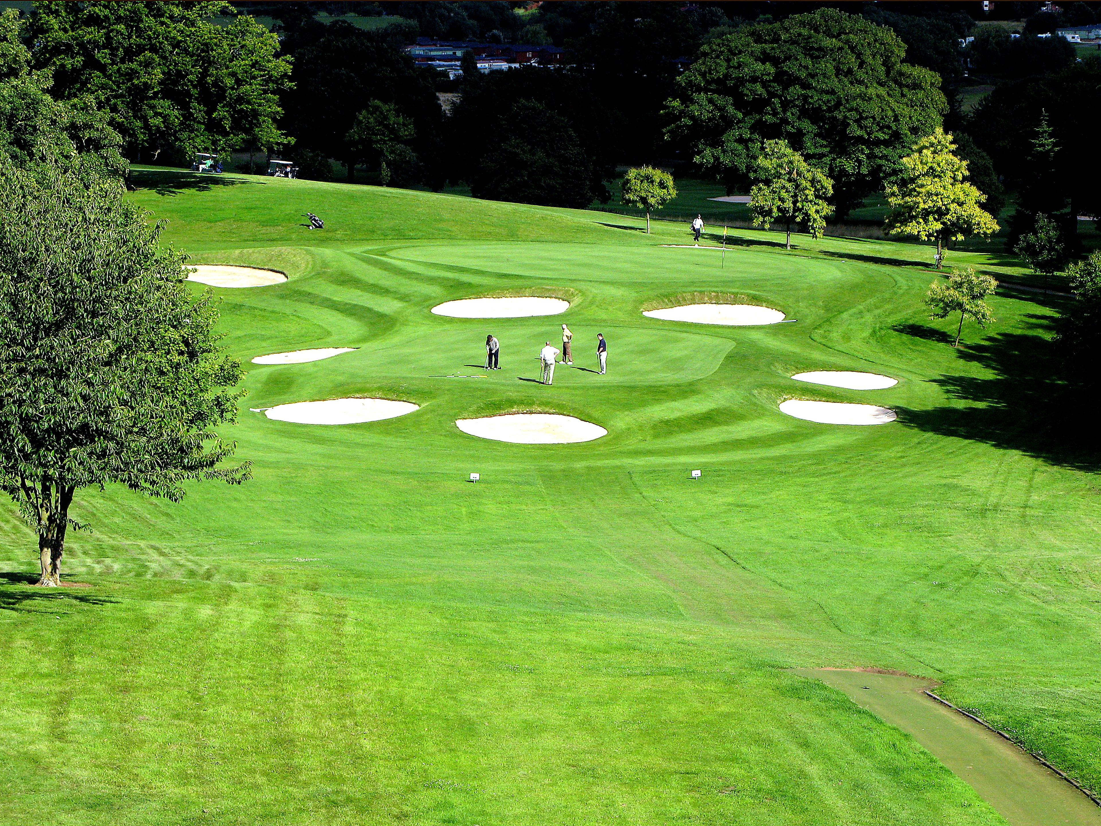 Un parcours de golf avec des bunkers de sable, des arbres et un ciel dégagé.