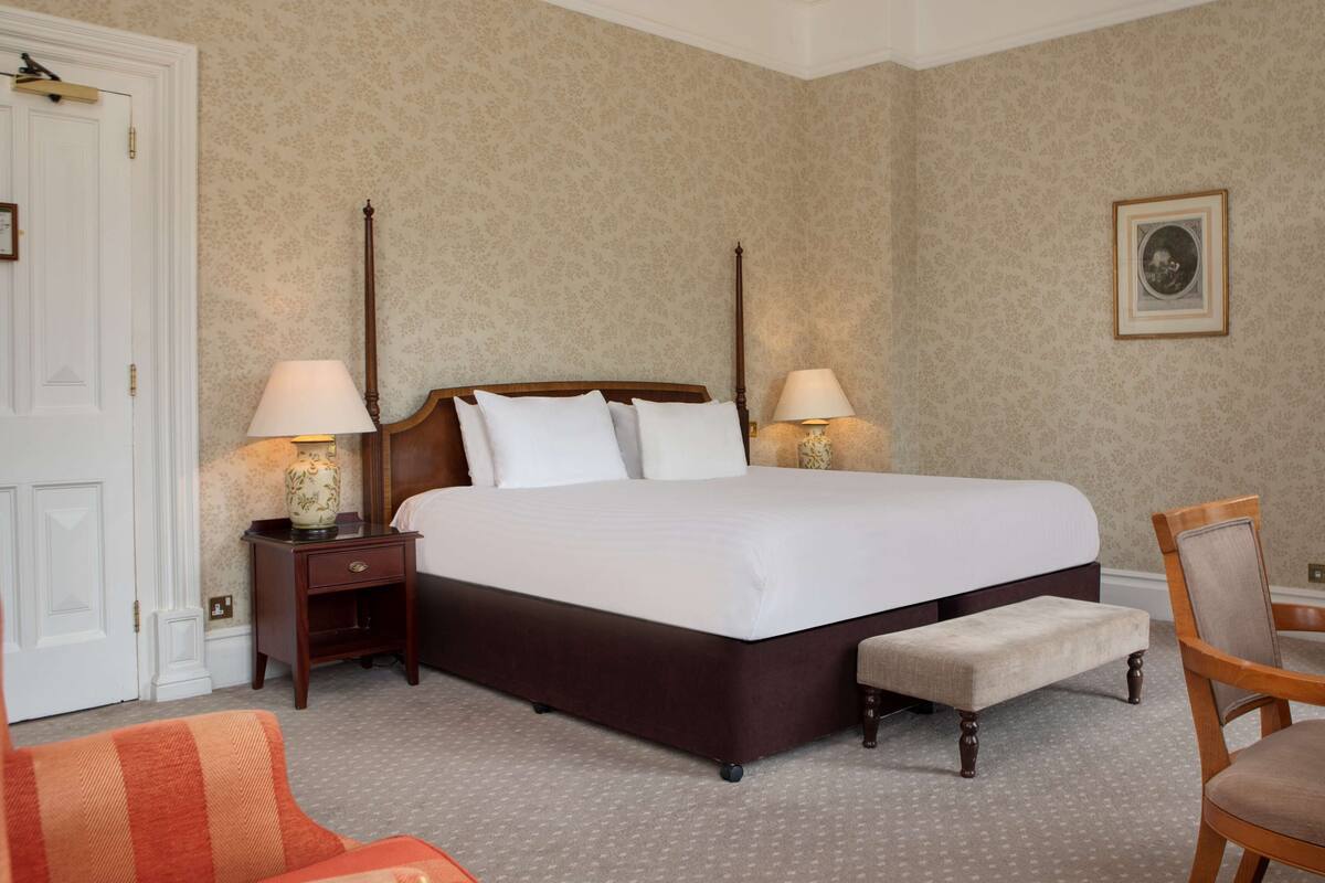 A neatly arranged bedroom with a large bed, two bedside tables with lamps, a chair, and a door.