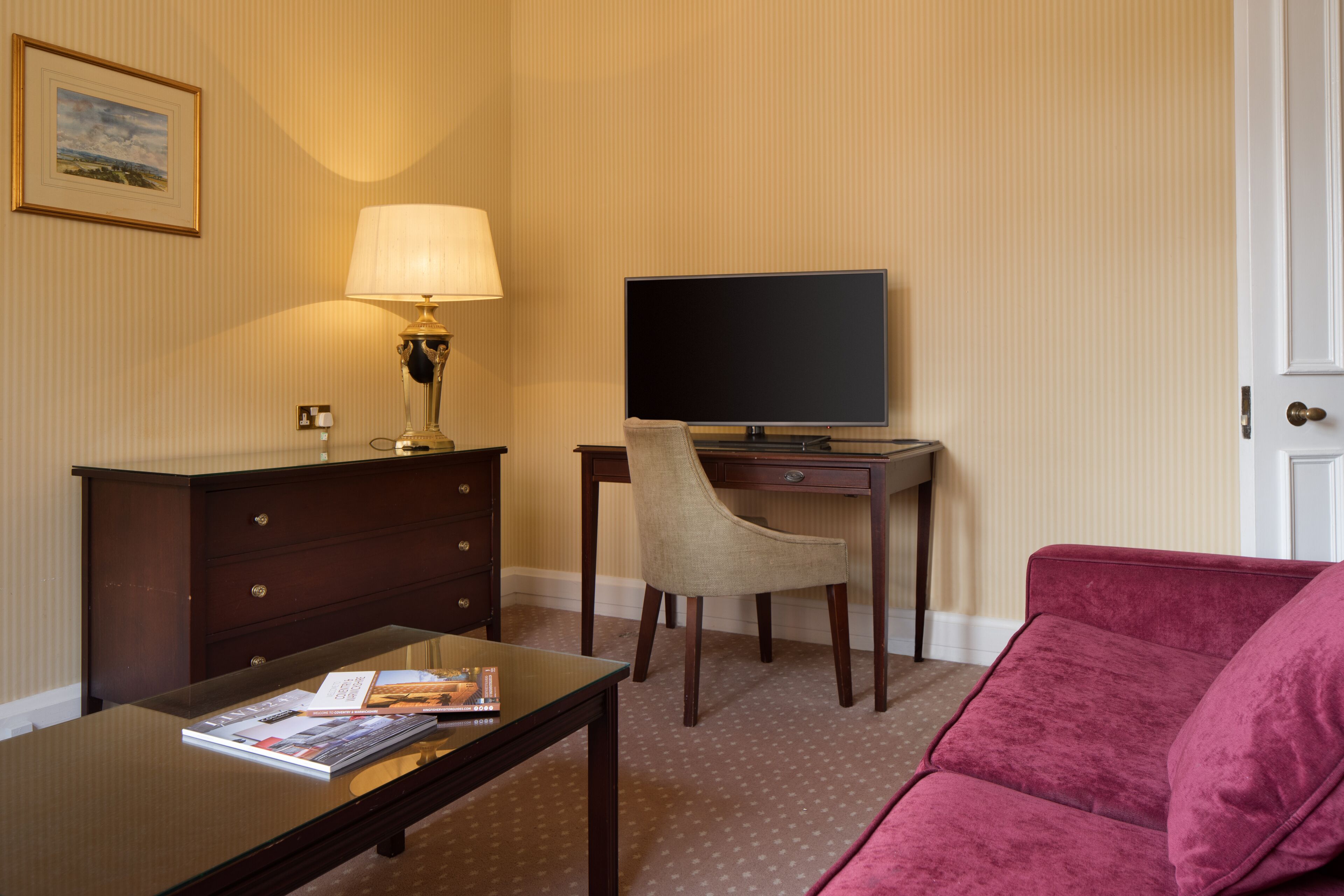 Hotelkamer met bureau, stoel, televisie en een rode bank.