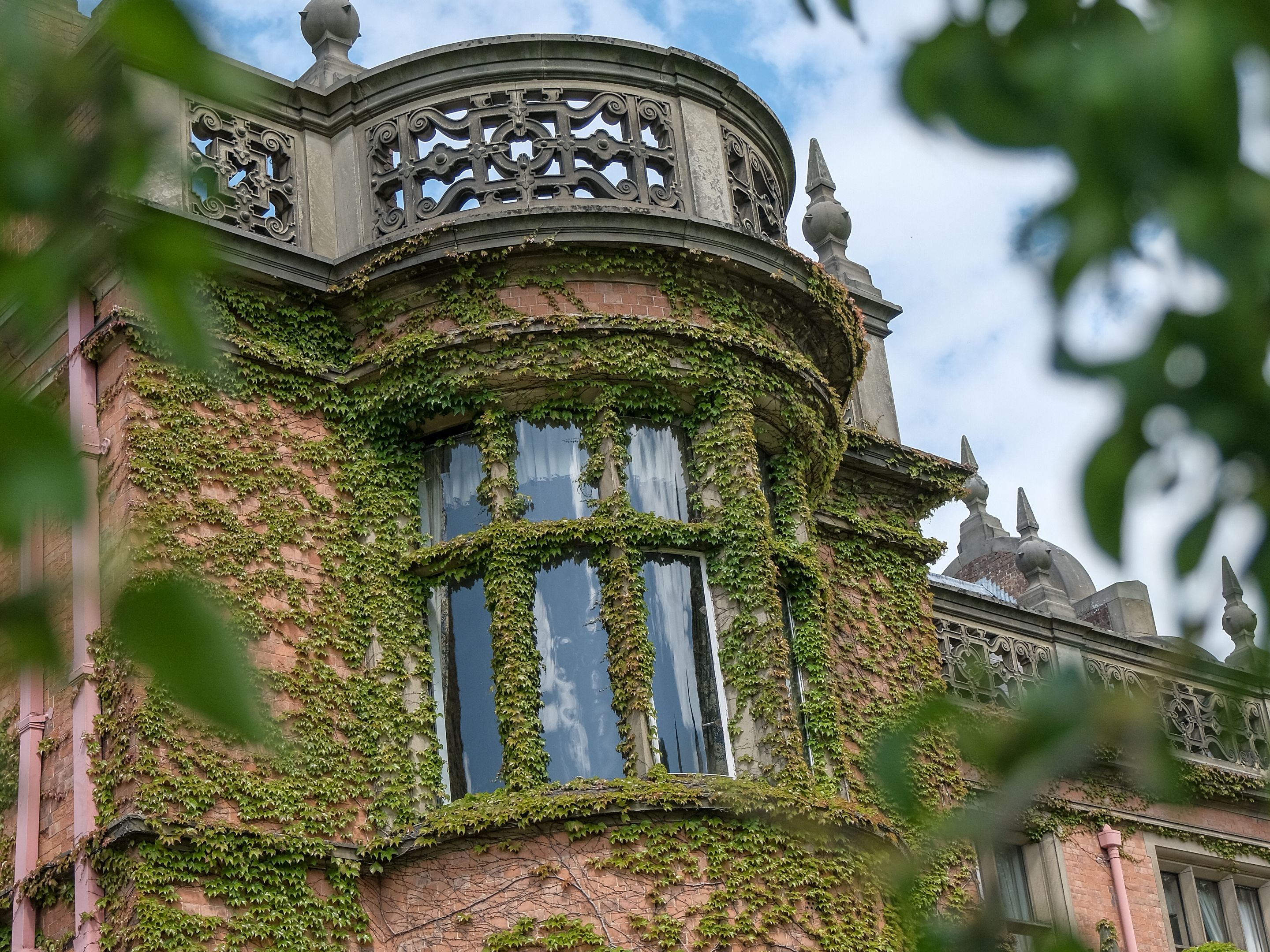 A building with a curved facade covered in ivy, large windows, and ornate ironwork.