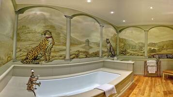 A bathroom with a large bathtub, a mirror, and a leopard mural on the wall.