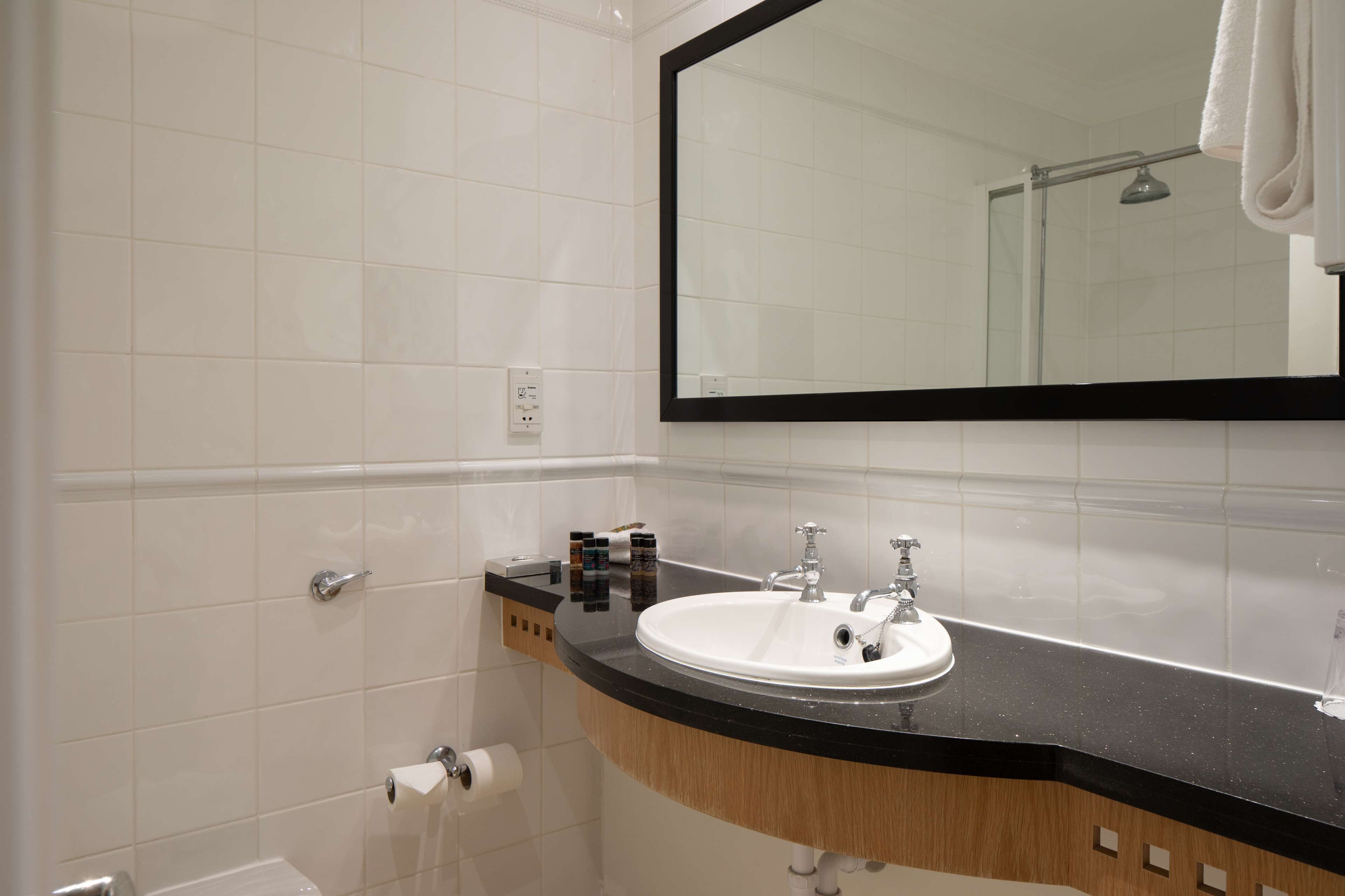 Une salle de bain avec un lavabo blanc, un plan de toilette noir et un grand miroir.