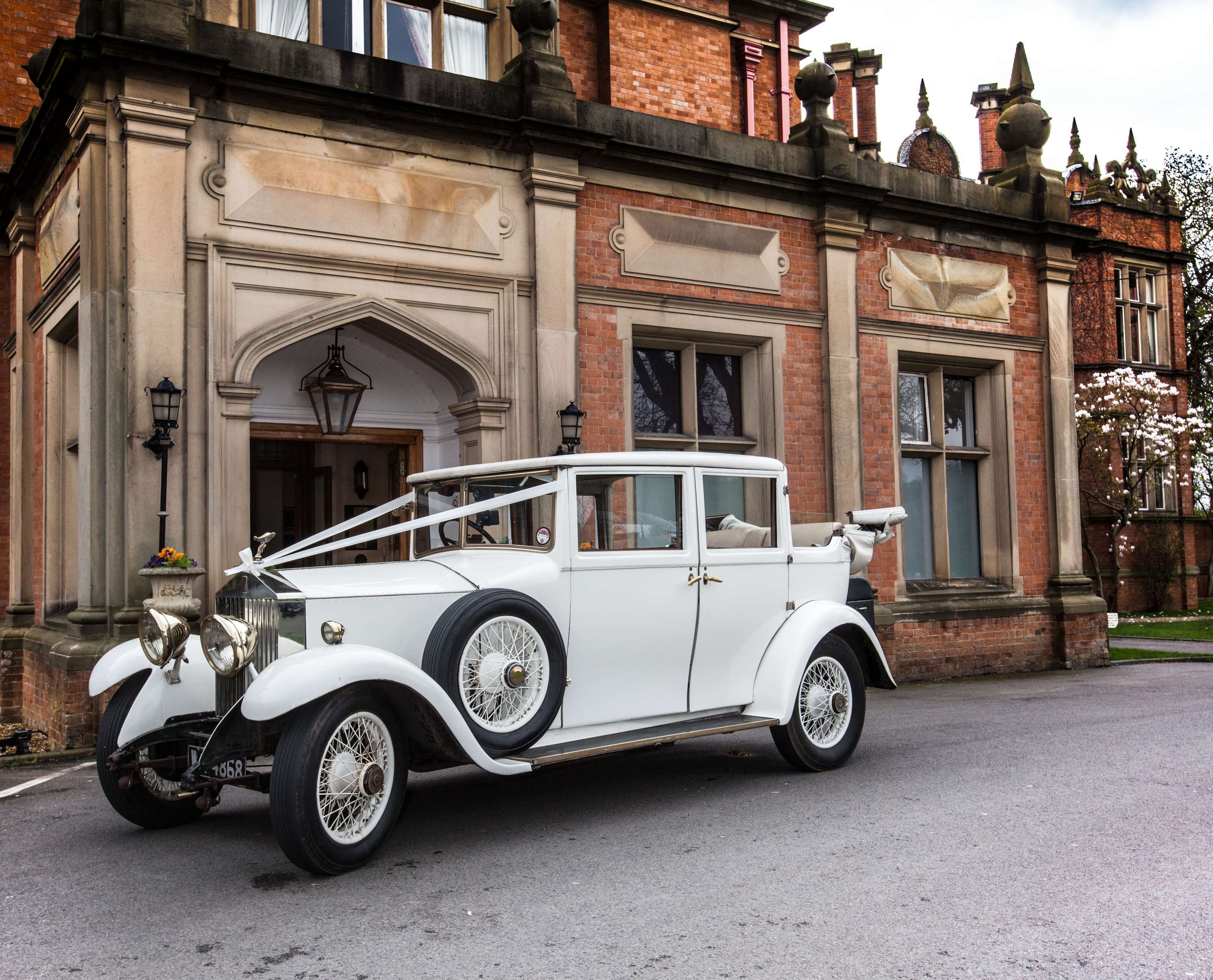A classic white car parked in front of a historic building with ornate architecture.