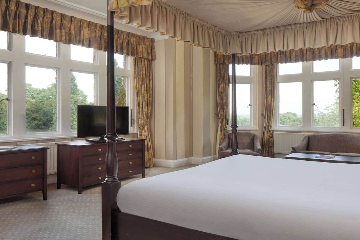A bedroom with a large bed, a dresser, a television, and two armchairs.