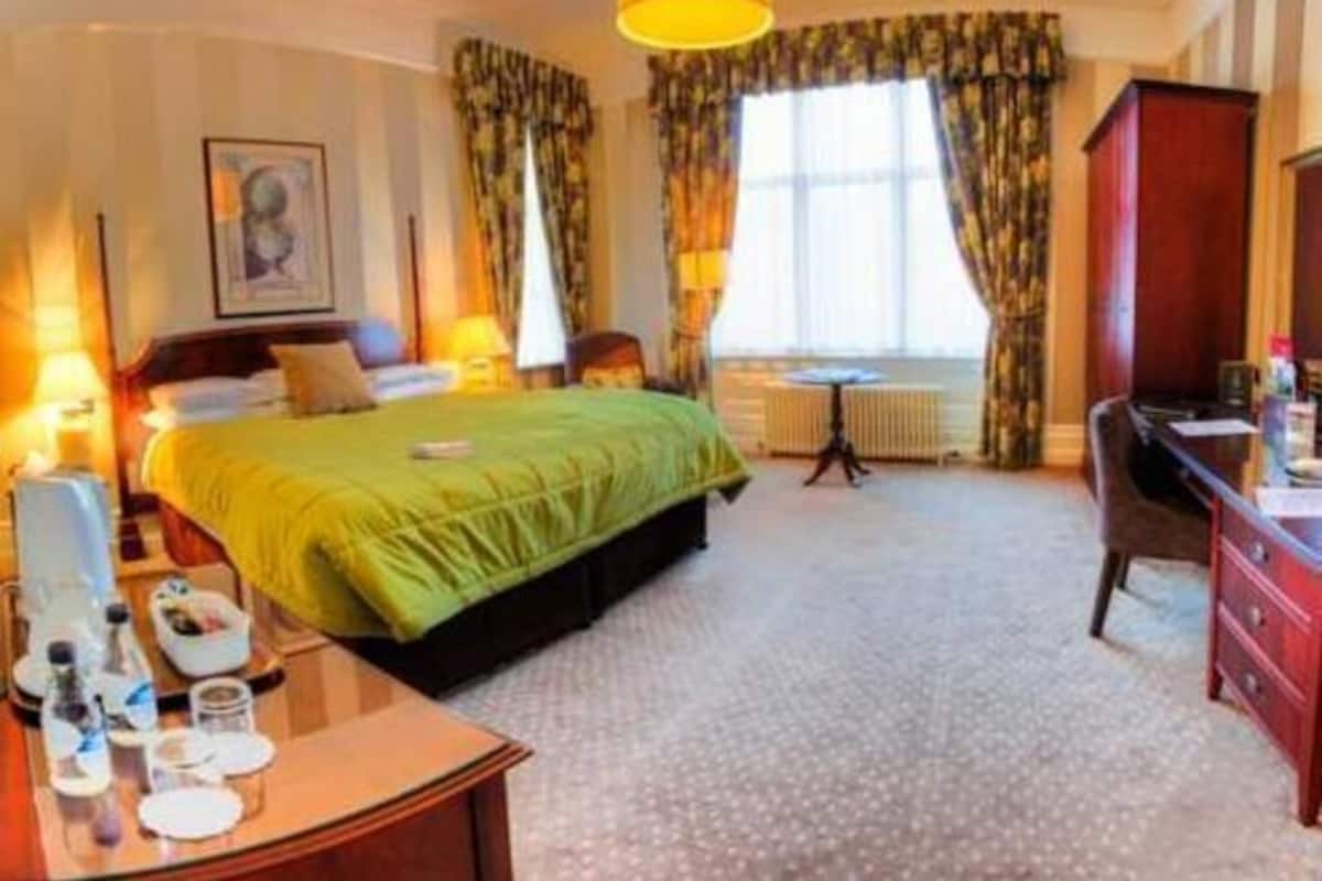 A hotel room with a bed, bedside table, lamp, and a window with curtains.