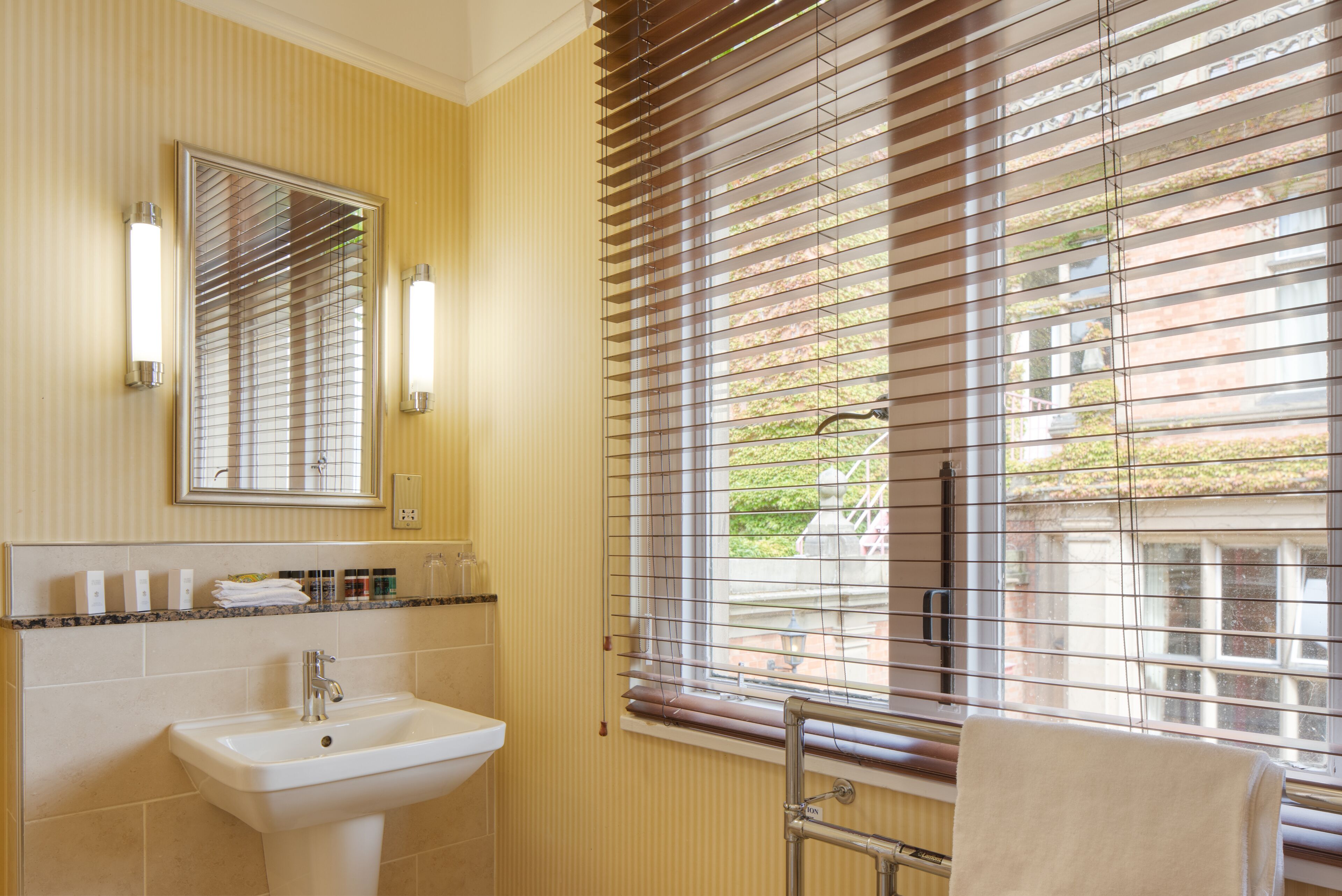 A bathroom with a sink, mirror, and window with blinds.