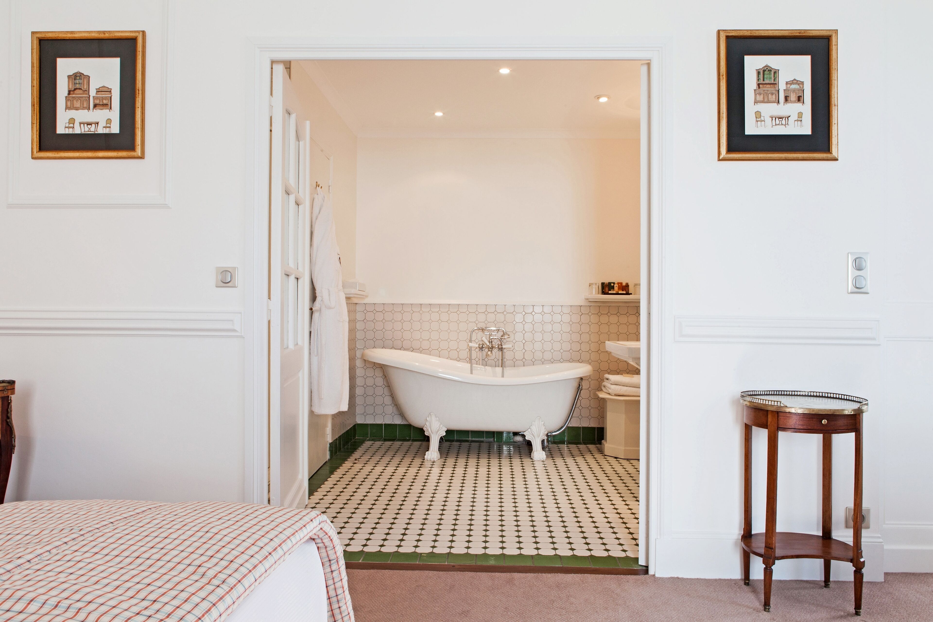 A bathroom with a freestanding bathtub, a sink, and a mirror. There is a framed picture on the wall and a small round table.