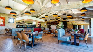 A spacious restaurant with high ceilings, exposed beams, and multiple hanging pendant lights. Tables and chairs are arranged for dining, with a bar area in the background. - Château des Vigiers (Monestier)