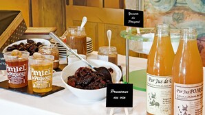 A buffet table with various food and drink options, including jars of preserves, bottles of juice, and a bowl of dark fruit compote. - Château des Vigiers (Monestier)