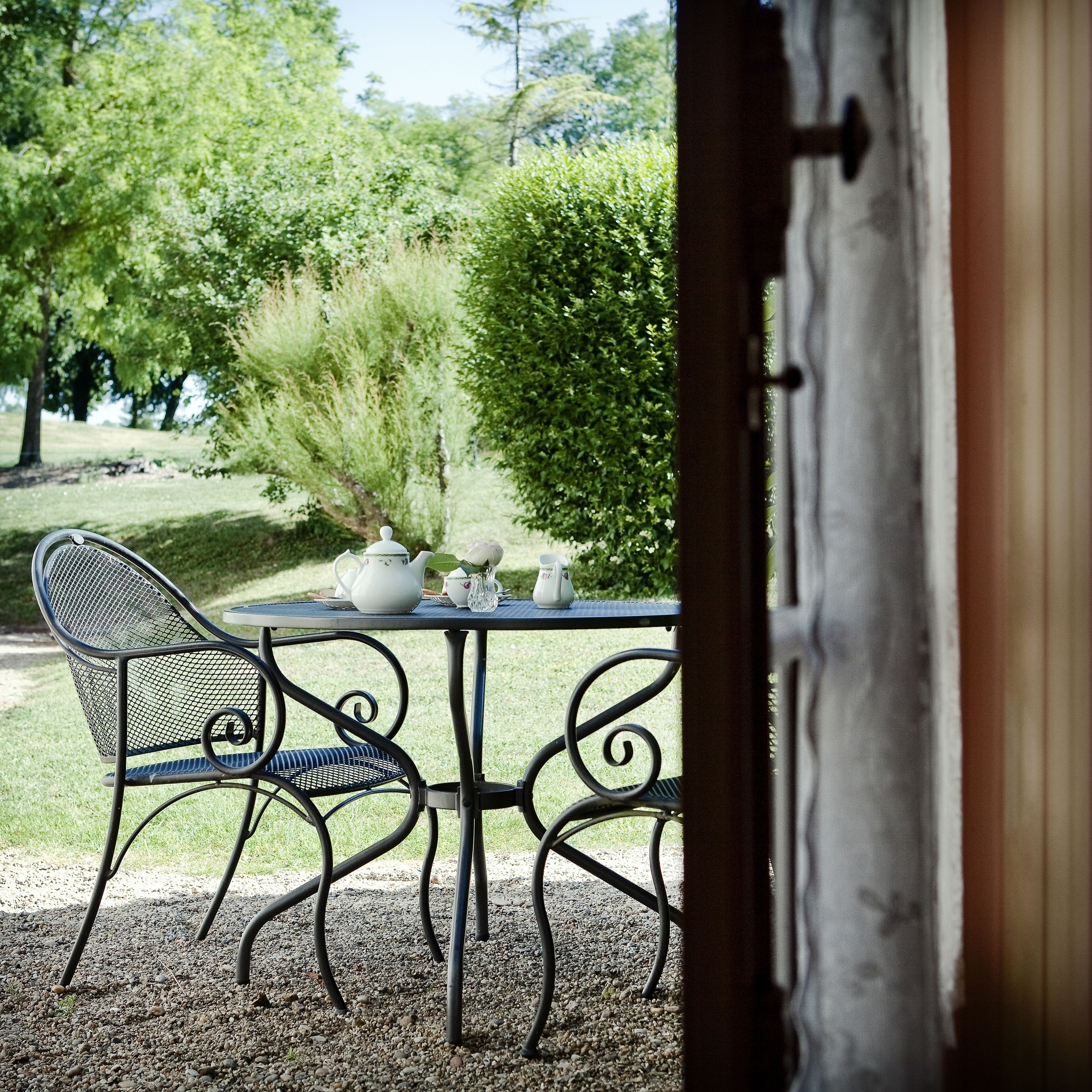 An outdoor seating area with a table and chairs, a teapot, cups, and a vase with flowers.