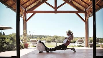 Een overdekt buitengebied met een houten dak, fitnessapparatuur en zitplaatsen.