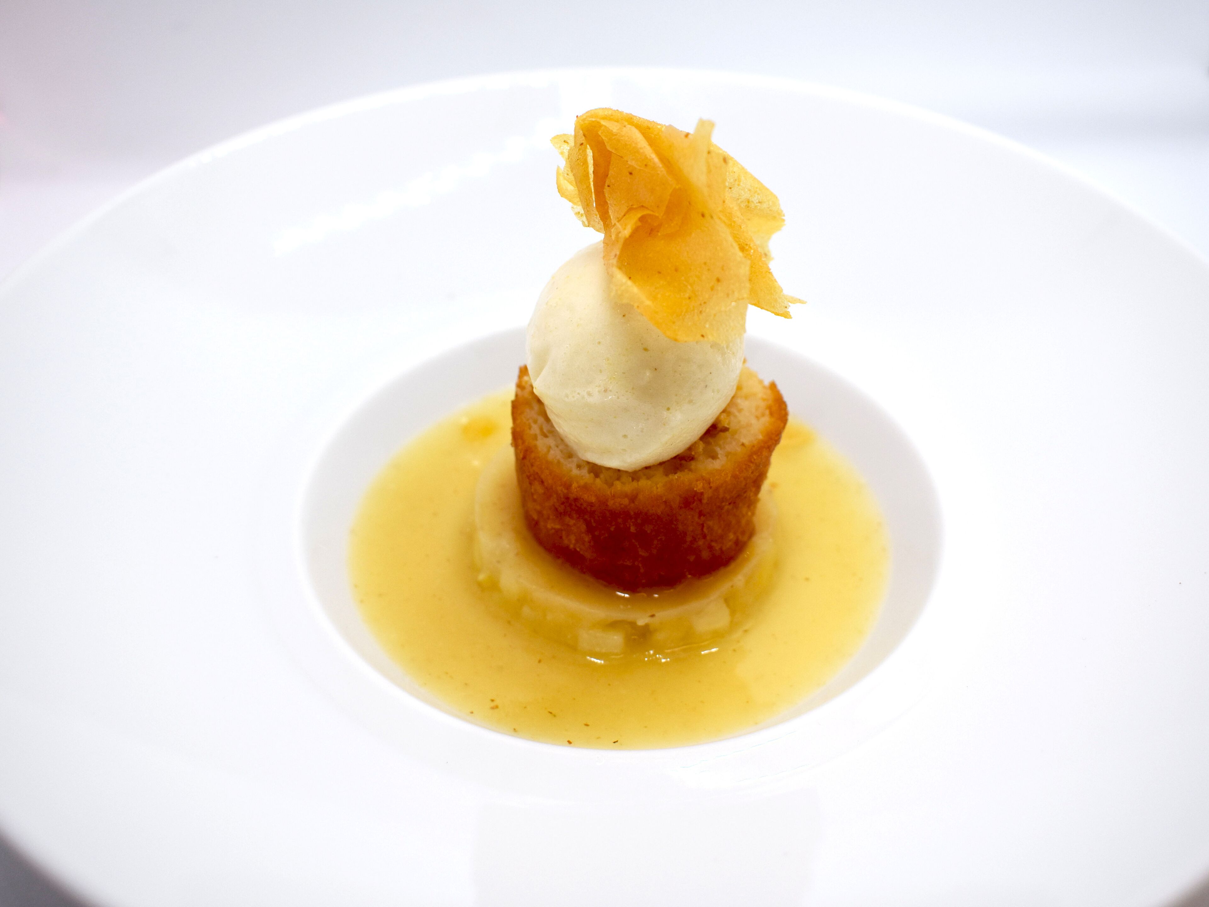 Een dessert op een wit bord met een gekaramelliseerde topping en een bol ijs.
