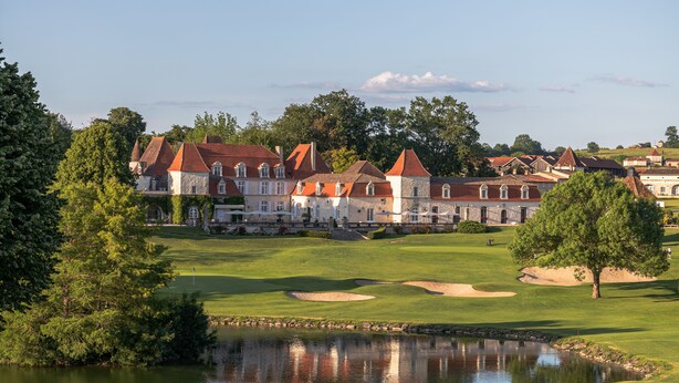 A golf course with a pond, trees, and a row of buildings with red roofs. - Château des Vigiers (Monestier)