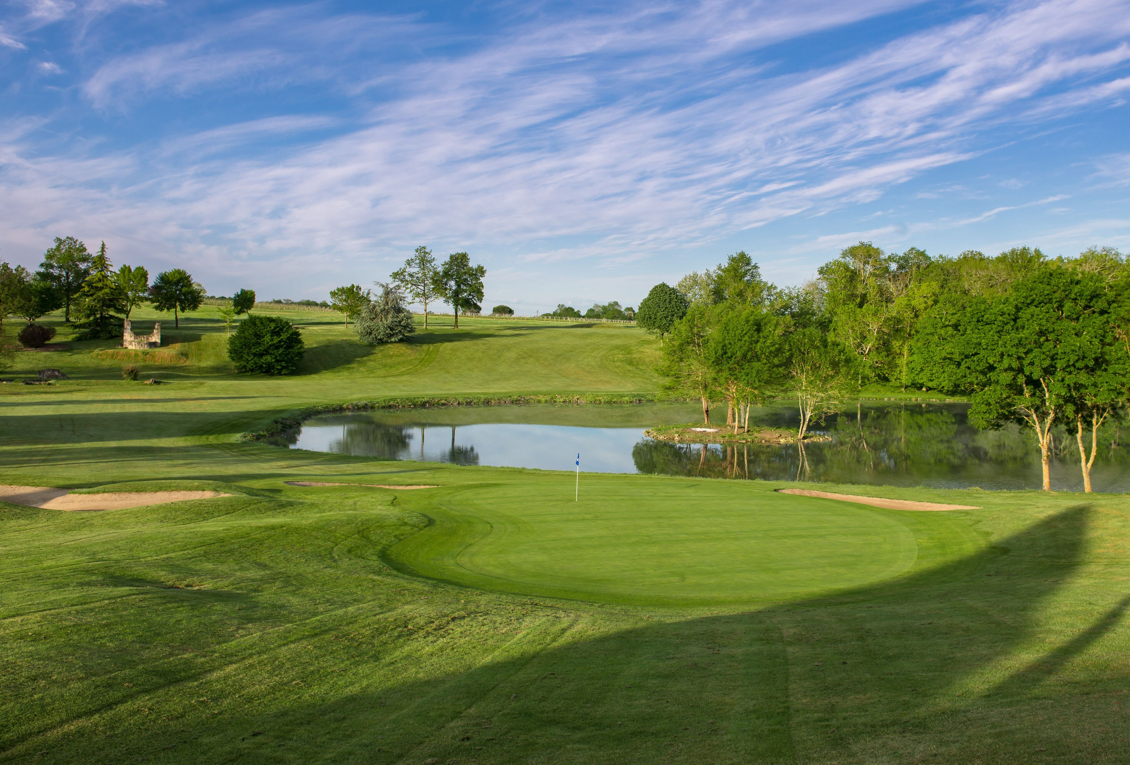 A golf course with a pond, trees, and a clear sky.