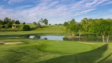 A golf course with a pond, trees, and a clear sky.