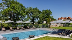 A rectangular swimming pool with lounge chairs and umbrellas, surrounded by a stone wall and greenery. - Château des Vigiers (Monestier)