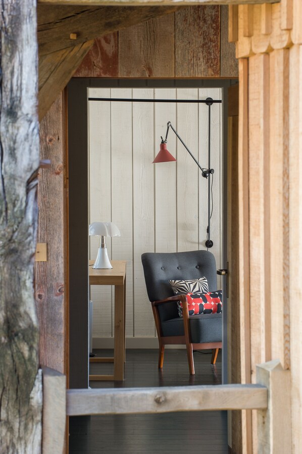 A cozy room with a wooden ceiling, a black chair with a patterned cushion, a small wooden table, and a white lamp.