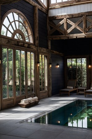 A spa area with a pool, wooden beams, large windows, and lounge chairs.