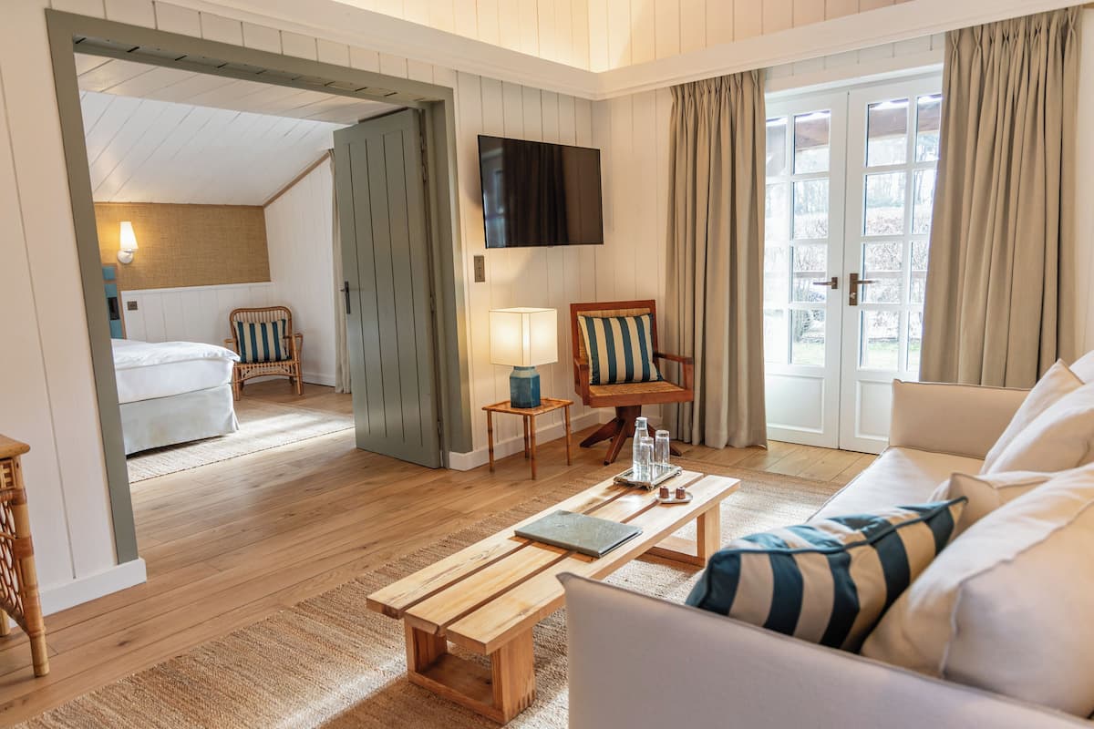 Une pièce avec un plancher en bois, un canapé, une table basse, un téléviseur fixé au mur et une porte donnant sur une autre pièce.