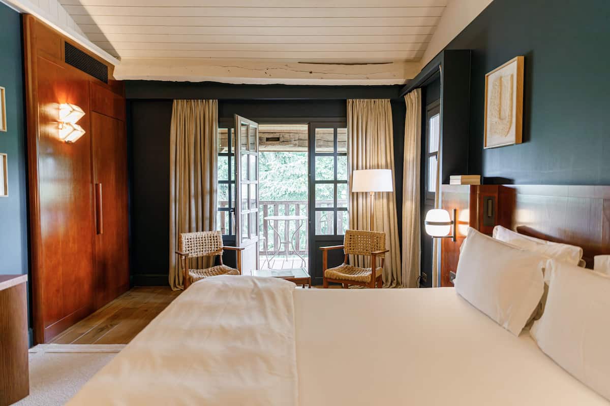 Une chambre avec un grand lit, deux fauteuils en osier, une petite table et une vue sur l’extérieur par une fenêtre.