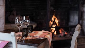 Mesa servida con copas de vino, cubiertos y una vela en una habitación acogedora con una chimenea al fondo.