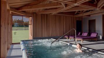 A spa area with a hot tub, wooden ceiling beams, and lounge chairs.