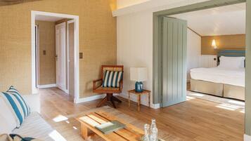 A hotel room with a wooden floor, a bed, a chair, a small table, and a sofa.