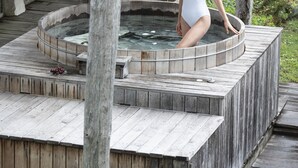 Un bain à remous en bois, doté d’une terrasse en bois rustique et d’un espace couvert avec un toit en tuiles.