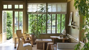 A sunlit room with a large window, a sofa, a chair, a table, and a potted plant.
