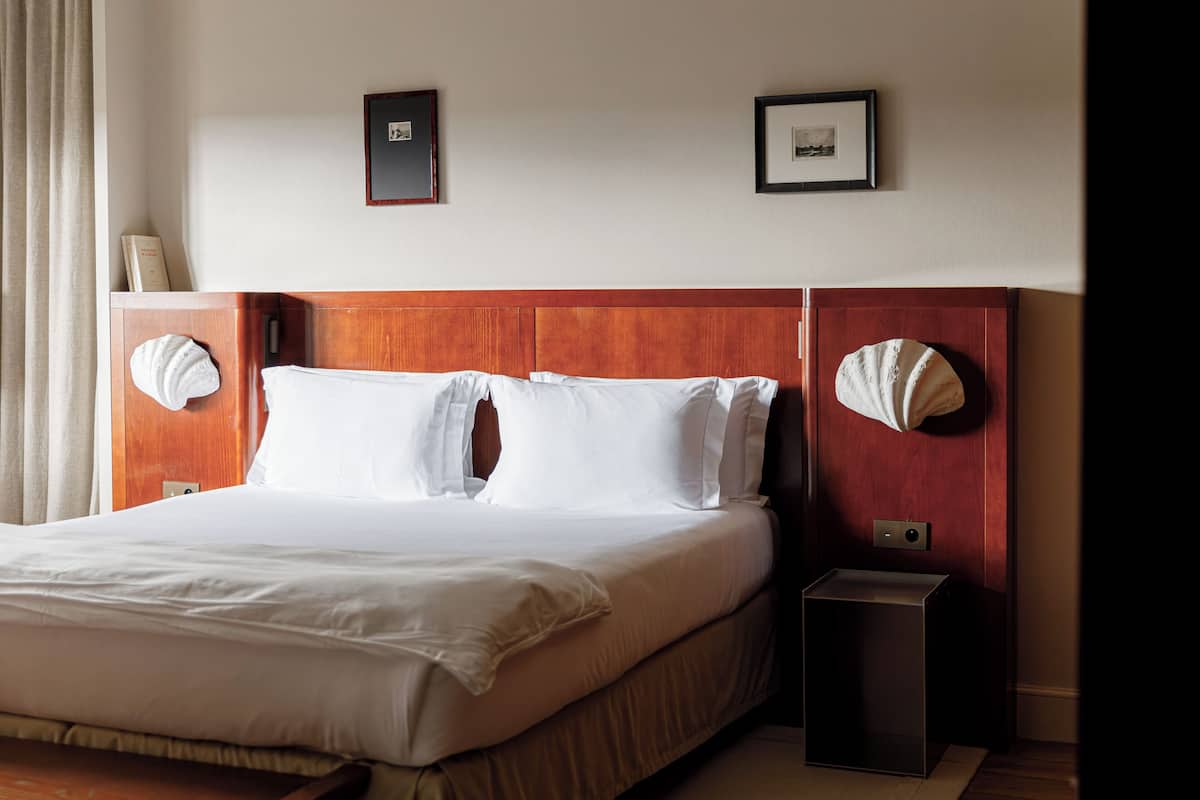 Une chambre d’hôtel avec un grand lit, une tête de lit en bois, deux tables de chevet avec des lampes et des tableaux encadrés accrochés au mur.