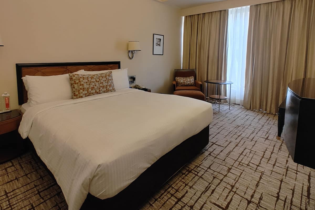 Quarto de hotel com uma cama grande, uma escrivaninha, uma cadeira e uma televisão.