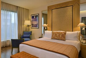 A hotel room with a large bed, two bedside lamps, a chair, a nightstand, and a mirror.