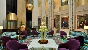 Eine Lobby mit einem runden Glastisch, violetten Sessel und einem Marmorboden.