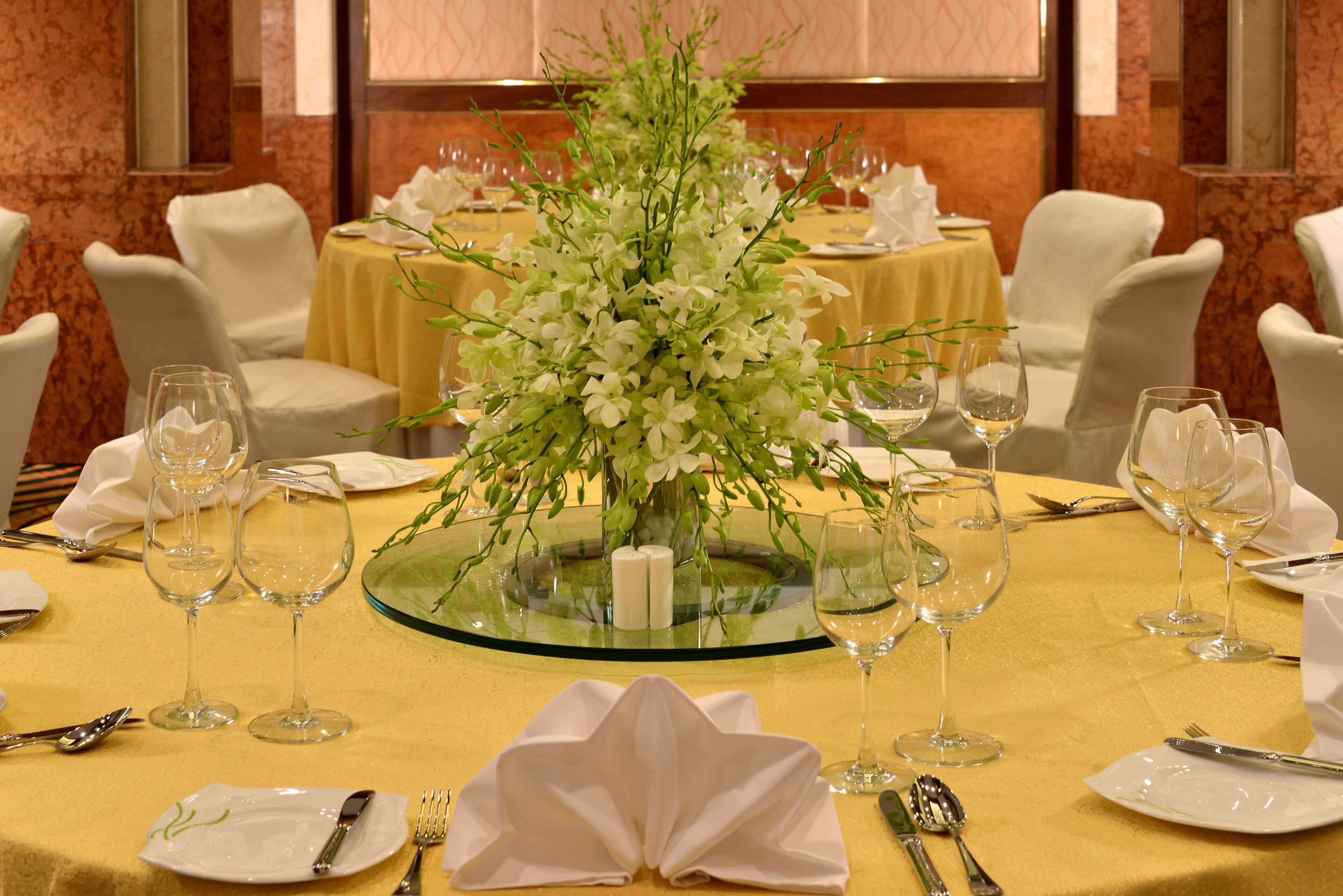 A formal dining setup with a central floral arrangement, white tablecloths, and neatly arranged glassware and cutlery.