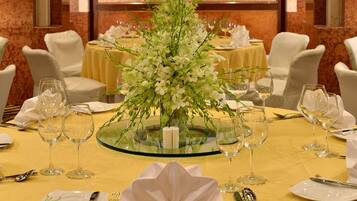 A formal dining setup with a central floral arrangement, white tablecloths, and neatly arranged glassware and cutlery.