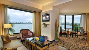 Ein Hotelzimmer mit großem Fenster und Blick auf die Stadt, einem Schreibtisch mit Laptop, einer Couch und einem Essbereich.