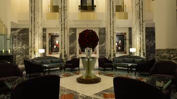 A lobby with a marble floor, a central table with a vase of red flowers, and two sofas facing the table.