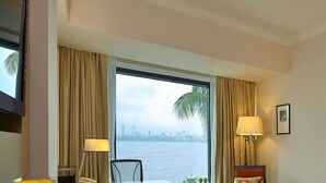 Ein Hotelzimmer mit großem Fenster, einem Bett, zwei Wandleuchten und Blick auf die Stadt.