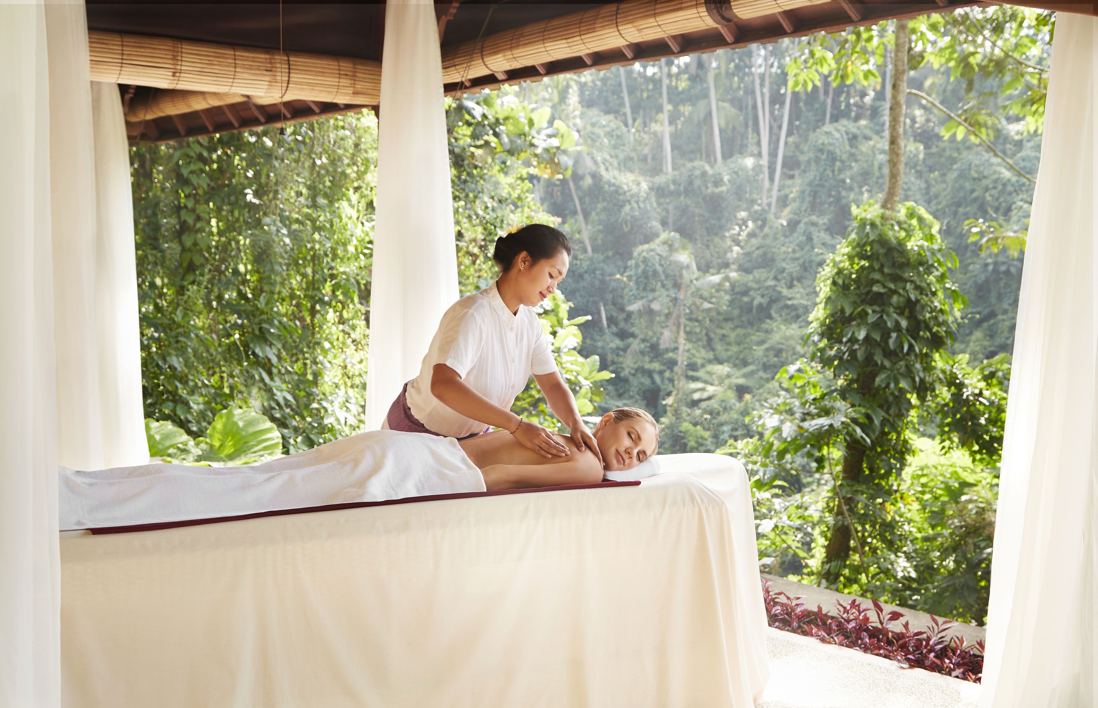 A massage therapy session in a room with a view of lush greenery.