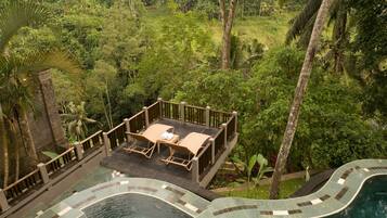 A pool area with a lounge chair and a small table, surrounded by lush greenery and palm trees.
